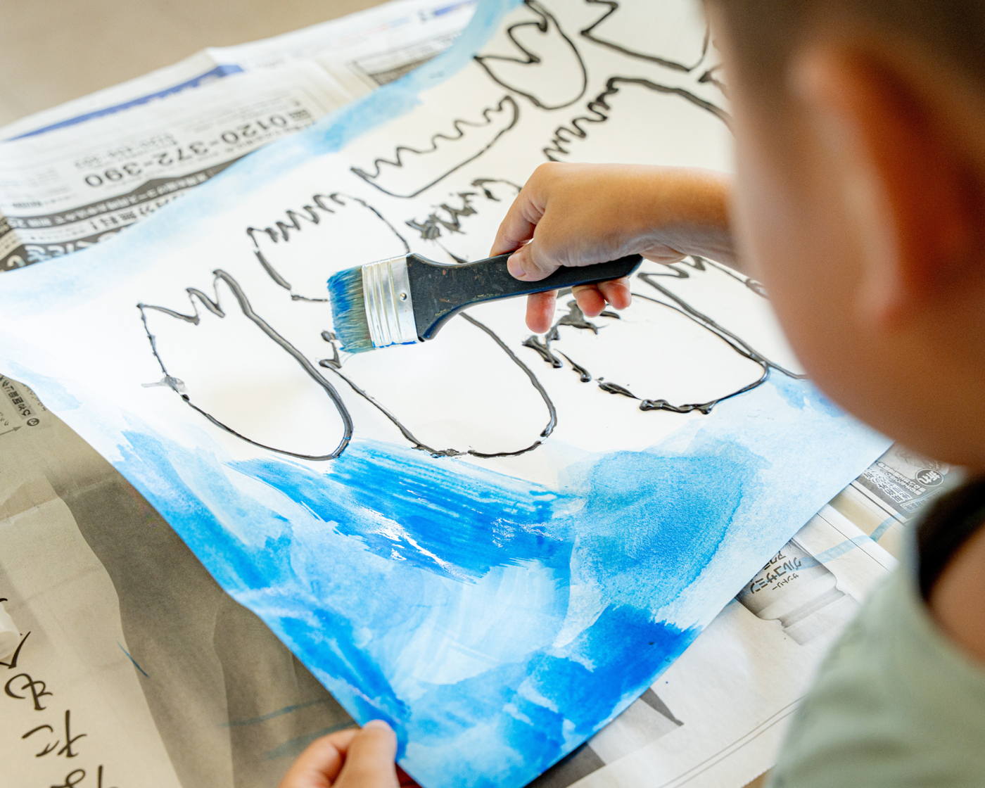 大きな筆で青い作品に色を重ねる子どもの手元
